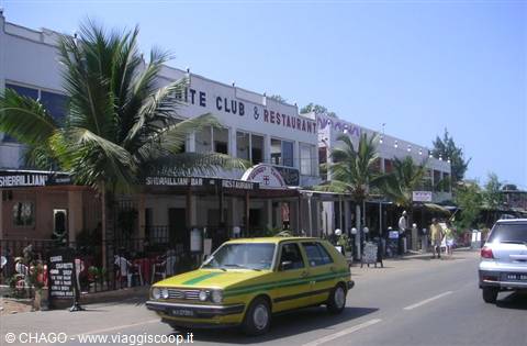 Yellow and green taxi in front of restaurants, palm trees, sunny street