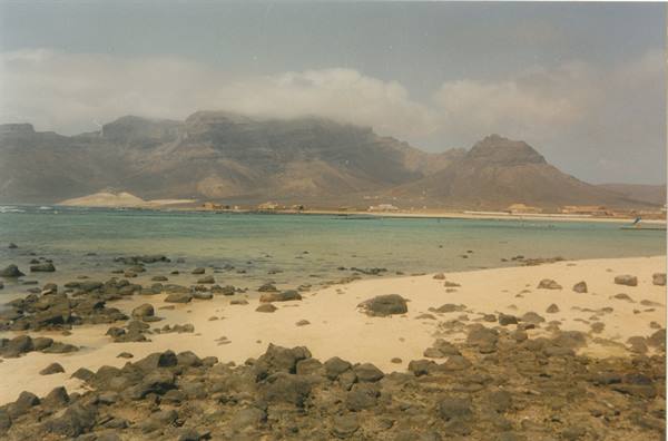 Sandy beach with rocks and low houses beneath volcanic mountains