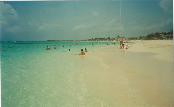 Swimmers in turquoise water on white sand beach under cloudy sky