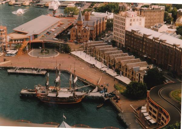 Tall ship moored at Sydney Cove wharf beside sandstone warehouses