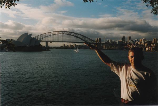 Man pointing at Sydney Harbour Bridge and Opera House, sailboat in the bay