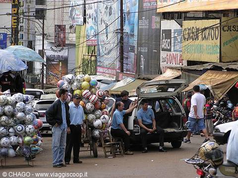 Vendor with cart of soccer balls beside taxis on a busy commercial street