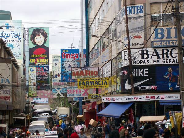 Busy street with colorful shop signs, pharmacy billboards, traffic and pedestrians