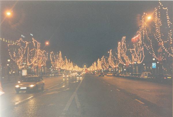 Avenue glowing with golden holiday lights, cars passing, distant arch: Champs-Élysées