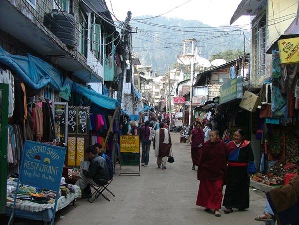 Monks in maroon robes walk through a market street, blue tarps and signs
