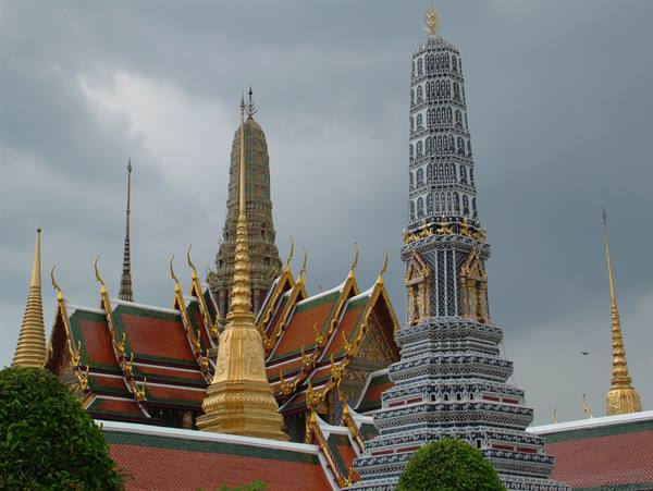 Gilded prangs and chedis of the Emerald Buddha Temple under stormy clouds