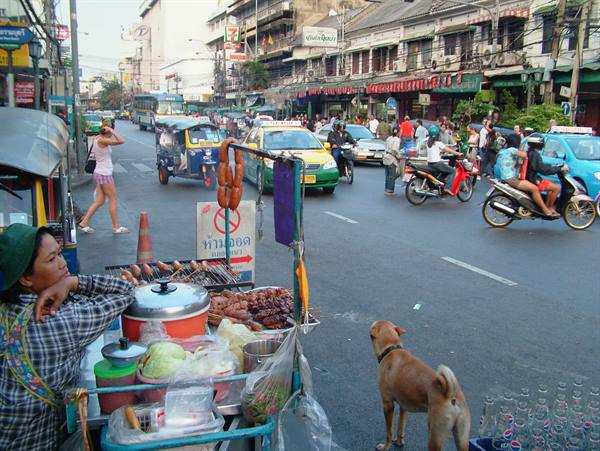 Street food vendor with cart, tuk-tuks and dogs amid Bangkok traffic