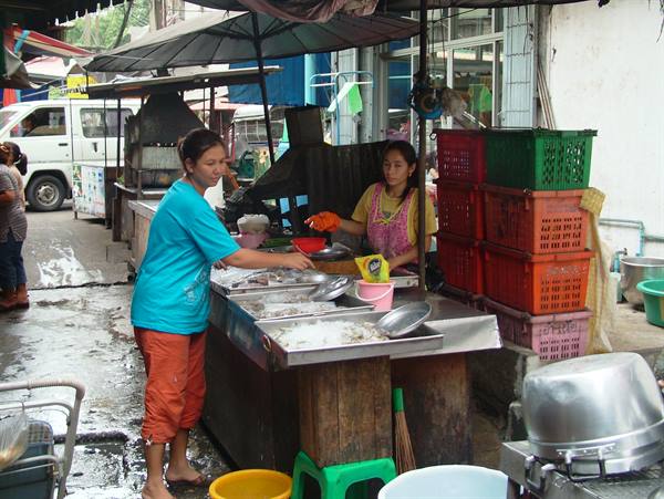 Woman at fish market trades goods with vendor beside colorful plastic crates