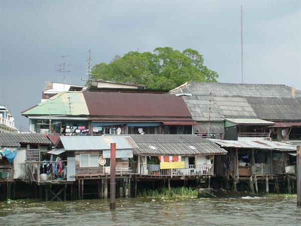 Wooden and tin stilt houses along the river, laundry hanging, grey sky