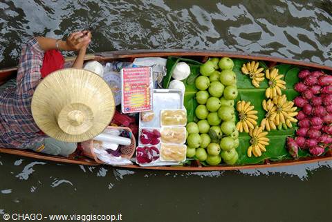 Vendor in straw hat on boat loaded with fruit, floating market