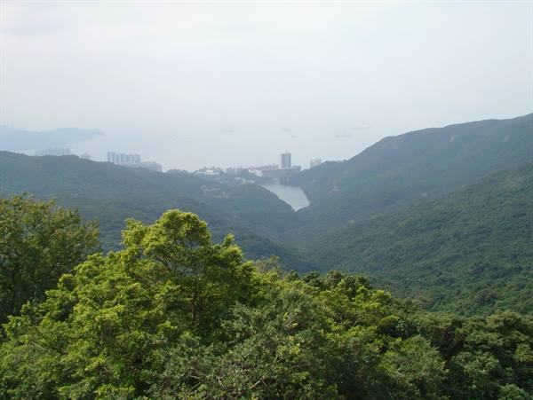 Lush green hills and hazy sky above a reservoir and distant city buildings