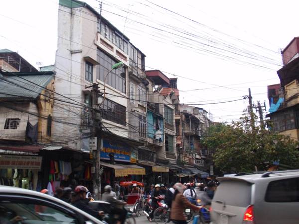 Motorbikes and cars in traffic among narrow buildings with tangled power lines, Hanoi