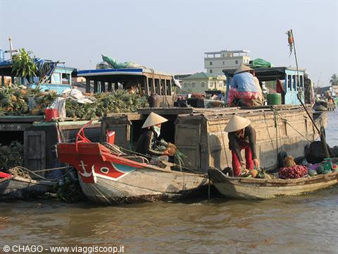 Women in conical hats selling fruit from wooden boats at floating market