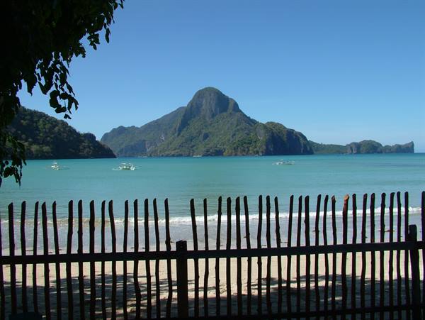 Wooden fence on beach, boats and green mountain over turquoise sea