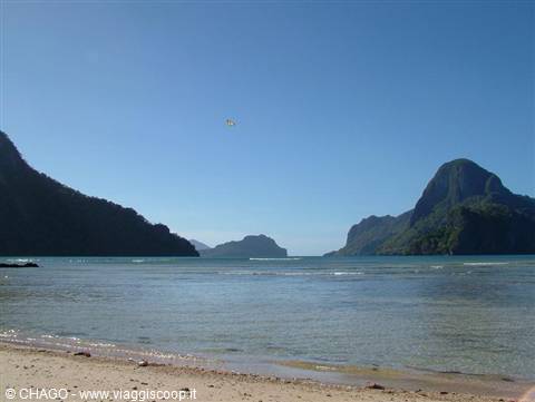 Pale sandy beach in front of green limestone cliffs, kite in blue sky, El Nido