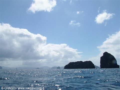 Black rock islets rise from the blue sea under white clouds