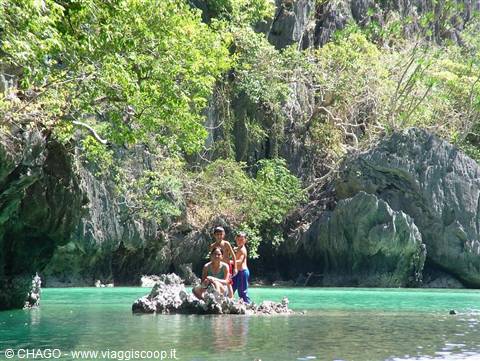 Three people on a rock in a turquoise lagoon among limestone cliffs at El Nido
