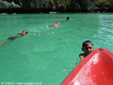 Children swimming in turquoise water beside a red boat