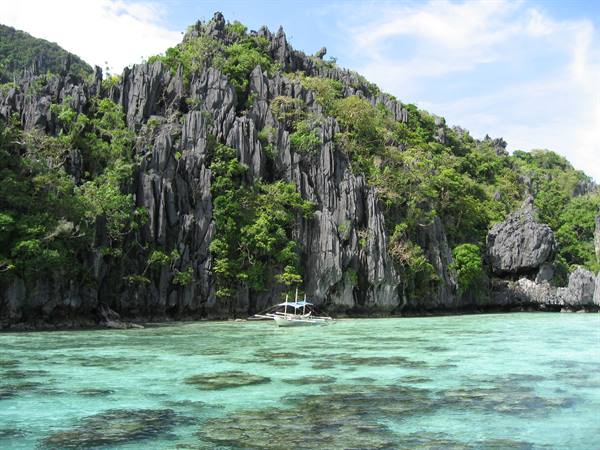 Boat moored on turquoise water beneath green limestone cliffs, El Nido, Palawan