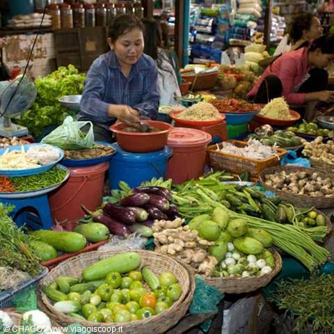 Covered market: vendor prepares food among baskets of eggplants, zucchinis and green papayas