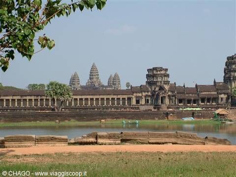 Angkor Wat: stone towers behind the pond, bright light, green branch in foreground
