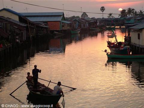 Fishermen rowing a wooden boat past stilt houses at dawn