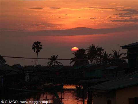 Red sun setting behind palms over the floating village on Tonlé Sap lake