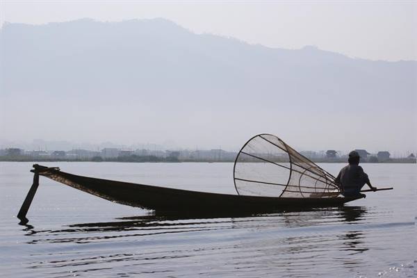 Fisherman on long canoe with conical net, Inle Lake, hazy light