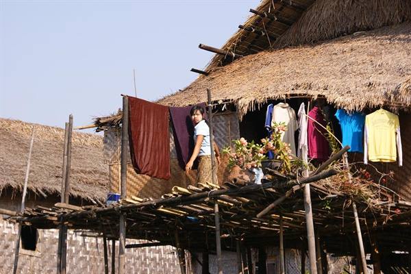 Girl on bamboo balcony of stilt house, laundry hanging, thatched roof
