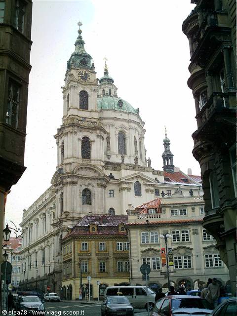 St Nicholas Church in Prague, green dome and baroque bell tower among buildings, street traffic