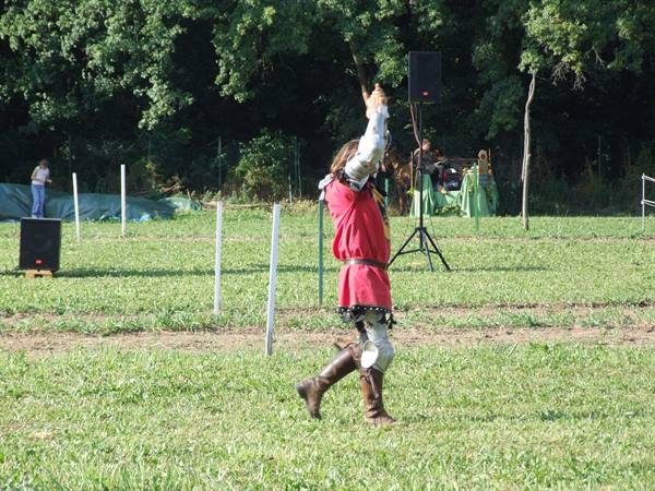 Knight in red tunic waves to the crowd at a medieval reenactment on the field