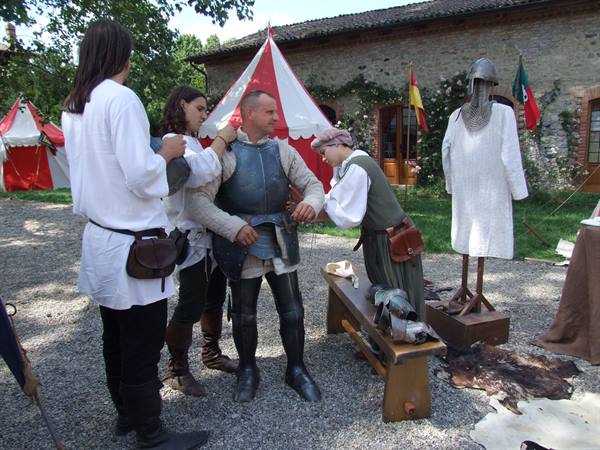 Medieval reenactment: men fitting a steel breastplate on a knight near tents