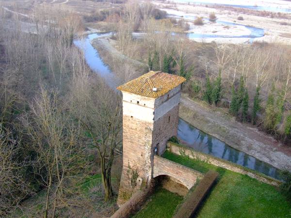 Old stone tower with tiled roof beside the river, bare trees