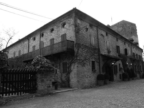 Stone building with wooden balcony, ivy and gate, in black and white