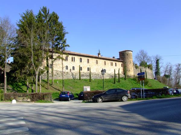 Medieval stone fortress with round tower, cars parked below the grassy slope
