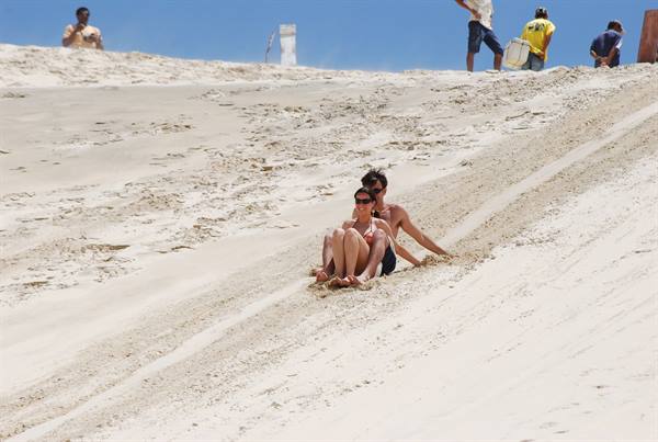Couple sliding down a white sand dune, tourists at the top
