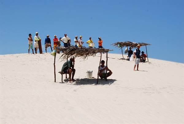 Vendors under straw shelters on white sand dune, blue sky