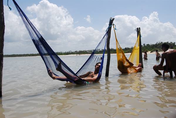 Men relaxing in blue and yellow hammocks over shallow beach water