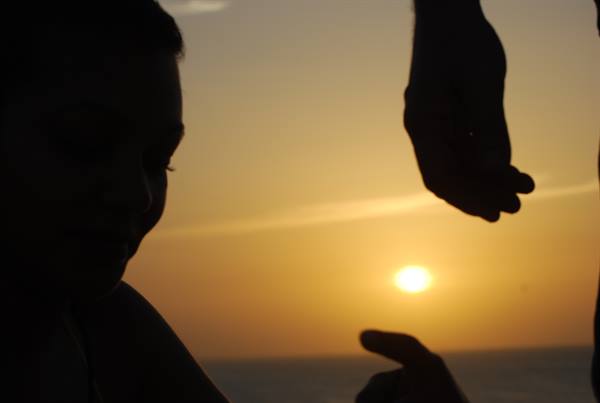 Child and hands silhouetted against the low sun over the sea