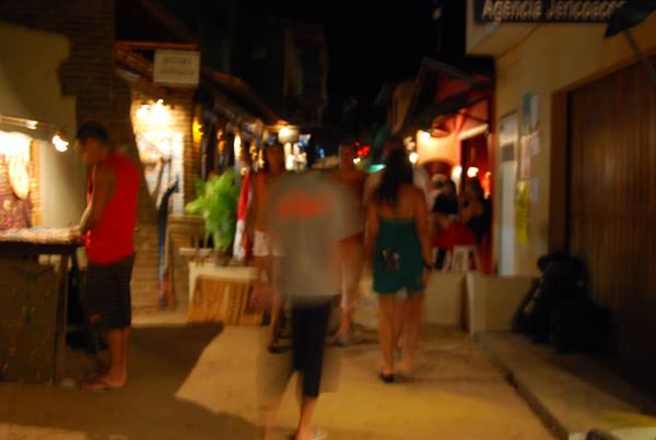 Blurred pedestrians walk at night among lit shops in Jericoacoara