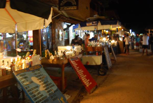 Night street bars with lit bottle stalls, menus and people walking around