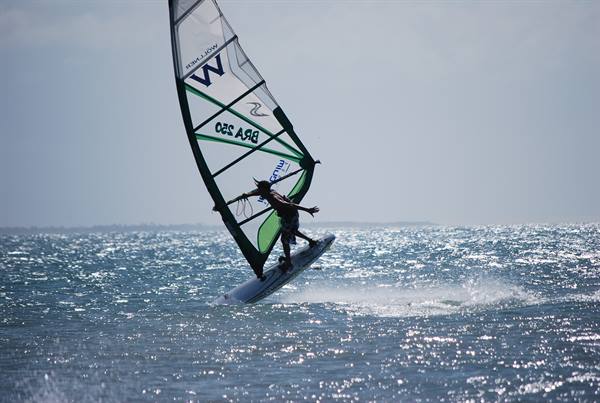 Windsurfer jumps over sparkling waves with green and grey sail