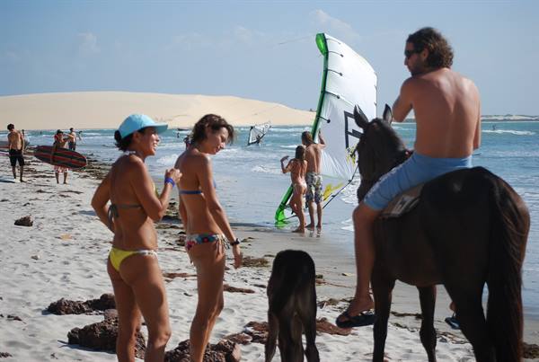 Horseback rider and beachgoers on sand, kiters prepare their kite by the water