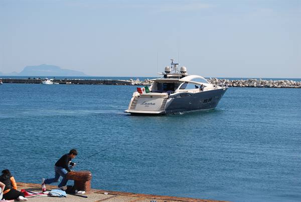 Child fishing from the pier while a yacht with Italian flag enters harbor