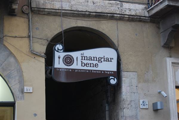 Sign of Al Mangiar Bene trattoria under a stone archway