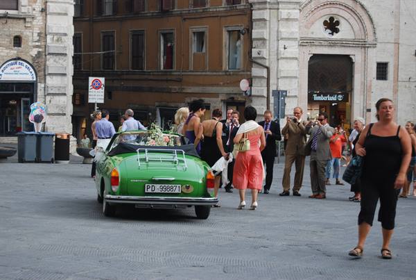 Newlyweds with flowers on a vintage green Fiat in a crowded square
