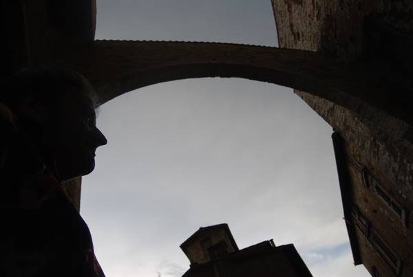 Silhouetted profile under a stone arch between old medieval brick buildings