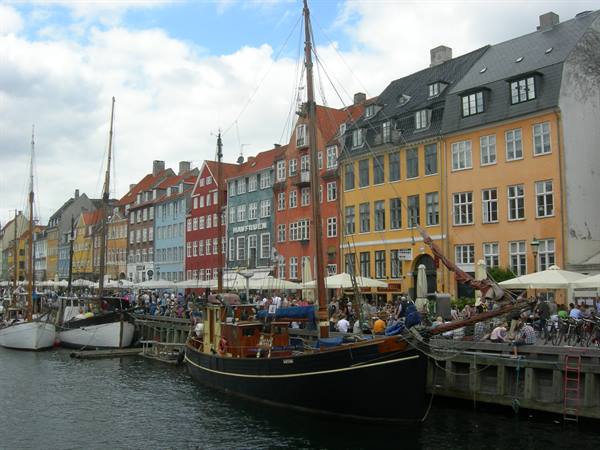 Wooden boat moored at Nyhavn, Copenhagen, colorful townhouses and people at cafes