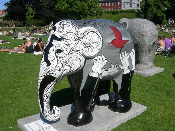 Painted elephant sculpture with hands and red bird in a busy green park