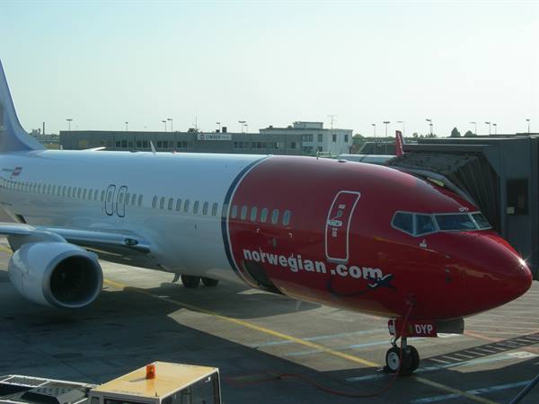 Red and white Norwegian airplane parked at airport gate with jet bridge